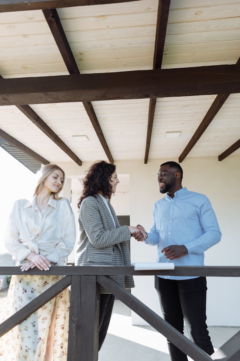 Two Anthony technicians on a residential porch with a homeowner, handshake moment